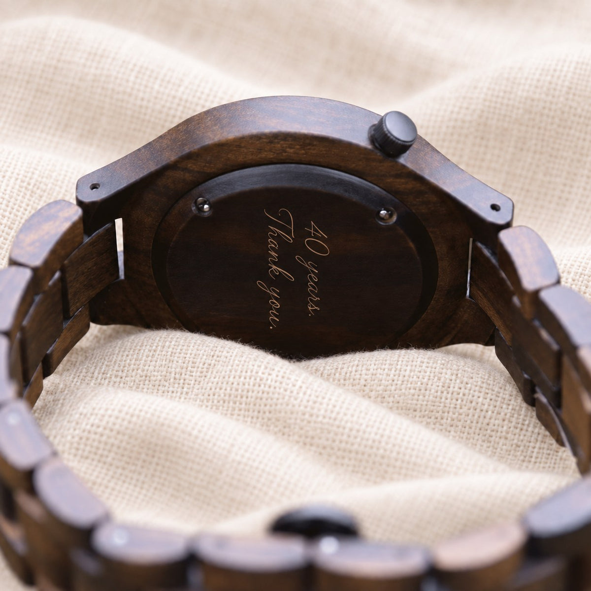 Nightfall wooden watch turned over on linen, its ebony caseback engraved with the words 40 years, thank you, in a script font