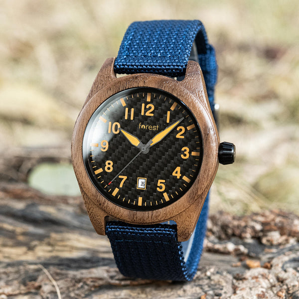 Scout wooden watch on a log, black dial with yellow numerals and blue fabric strap
