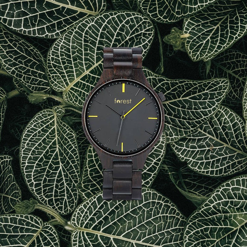 Umber black wooden watch on patterned green leaves