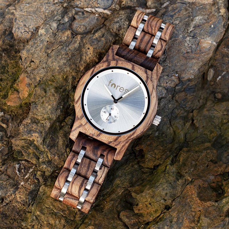 Alpine wooden watch laid open on mossy rock, zebrawood bracelet unfastened