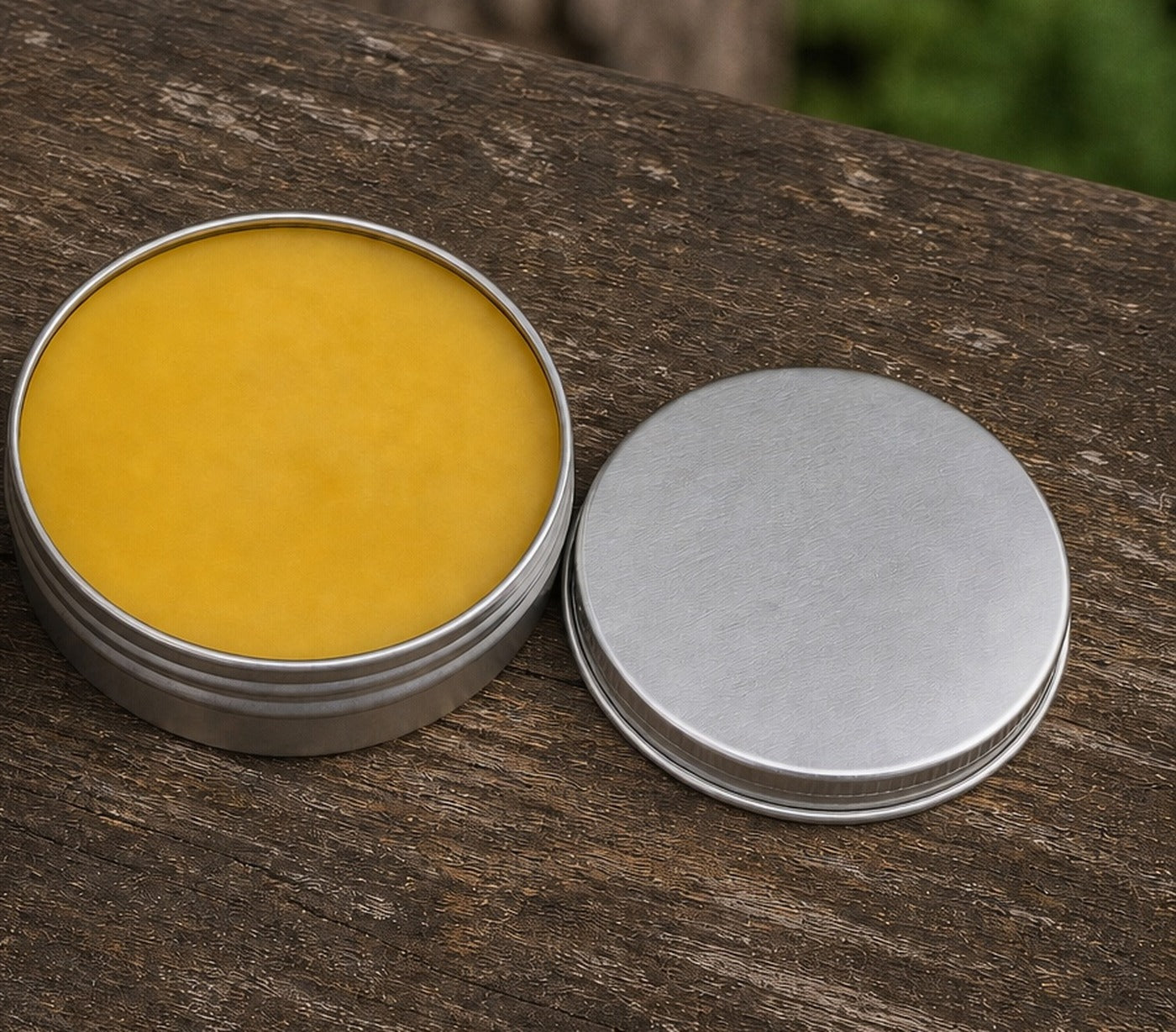 An open tin of natural beeswax wood wax beside its lid on a wooden bench