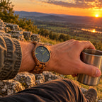 Dusk zebrawood watch on a man's wrist, holding a steel cup on a hilltop at sunset