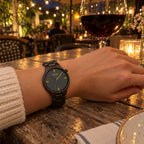 Nightfall ebony watch on a woman's wrist at a café table under string lights