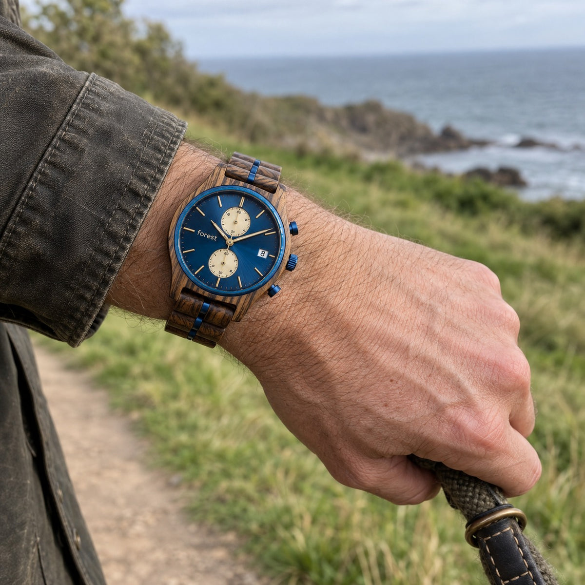Nightjar wooden watch on a man's wrist, hand holding a dog lead on a coastal path